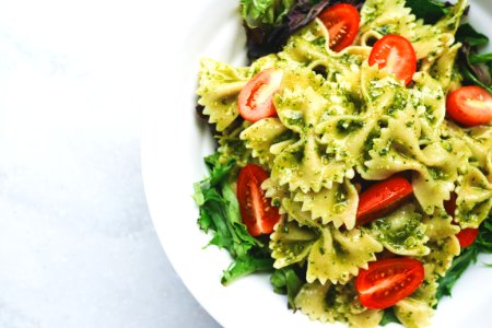 Pesto pasta with sliced tomatoes served on white ceramic plate photo