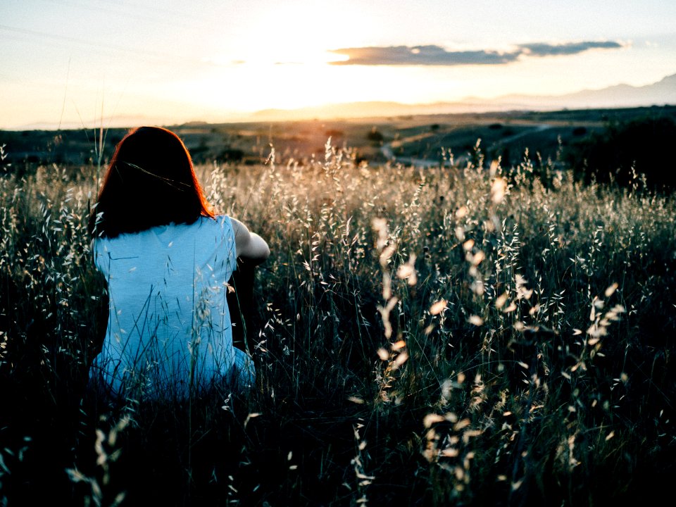 woman sitting on grass field watching sunset