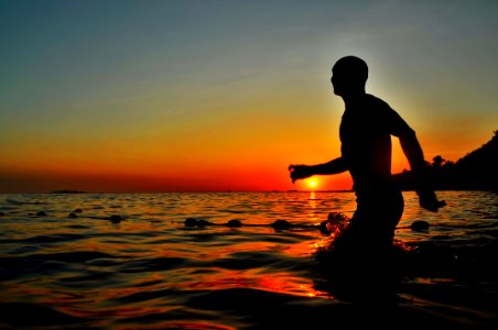 silhouette of man walking in body of water photo