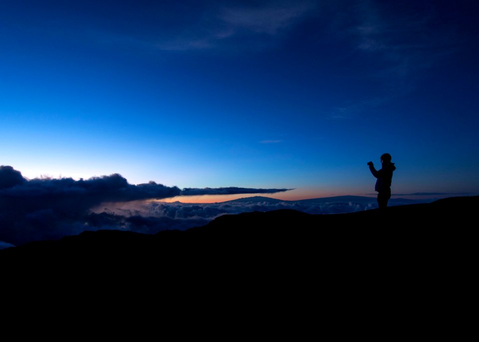 silhouette of man taking photo on rock cliff