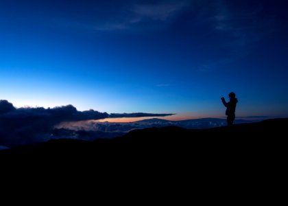 silhouette of man taking photo on rock cliff