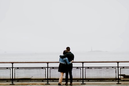 couple standing in front of fence near body of water photo