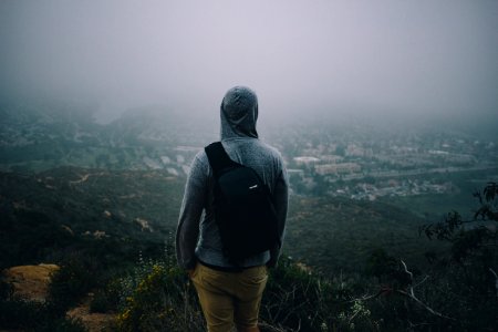 man in gray hoodie with black backpack looking at the city from mountain peek photo