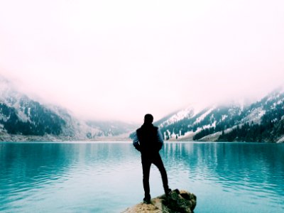 man standing on brown rock facing beside body of water photo