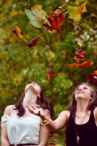 photo of two women throwing leaves during daytime