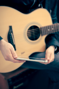 person with guitar on lap holding tablet photo