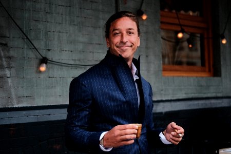 man wearing black suit holding brown mug near black string lights photo