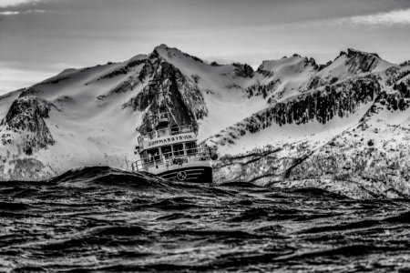 grayscale photography of ship on body of water near at snowy mountain photo