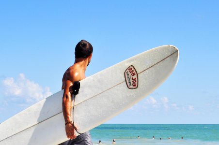 topless man carrying white surfboard in beach during daytime photo