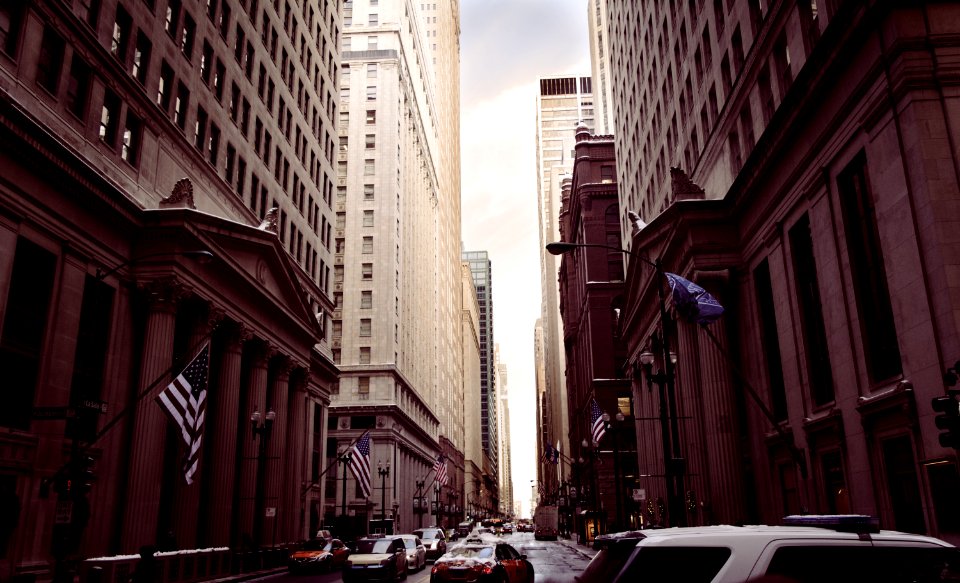 vehicles on concrete road between high buildings under white sky at daytime