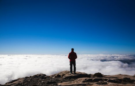 man standing on brown mountains facing sea of clouds photo