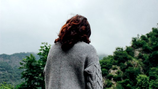 woman in gray sweater standing in front of trees during daytime photo