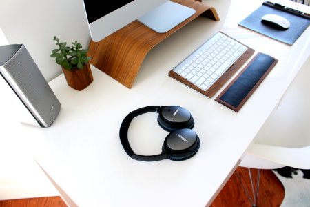 A desk with headphones, a keyboard and wrist wrest, monitor, mouse, speakers and a plant.