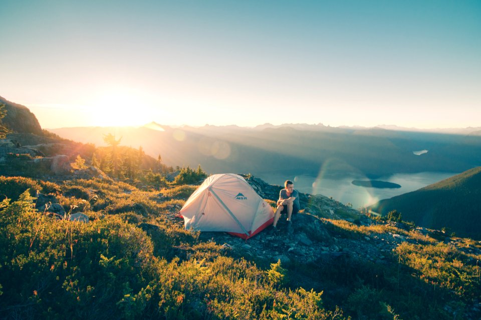 man sitting on stone beside white camping tent