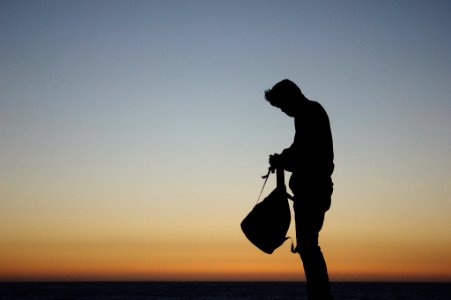 silhouette of man holding backpack during orange sunset photo