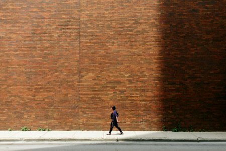 woman in black shirt walking on sidewalk near brown concrete wall partition photo