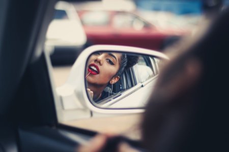 woman putting liquid lipstick on her lips while looking at vehicle's mirror during daytime photo