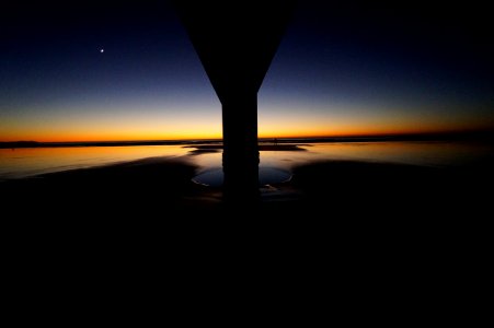 The sun-kissed horizon looms behind the pillar and across the water at dusk at New Brighton photo