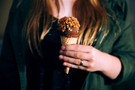 woman in green jacket holding chocolate ice cream coated of nuts during daytime shallow focus photography photo