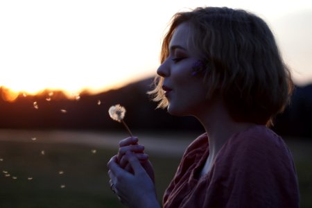 woman blowing dandelion flower selective focus photography photo