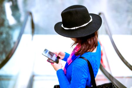 woman in blue and orange long sleeve shirt wearing black hat holding black smartphone