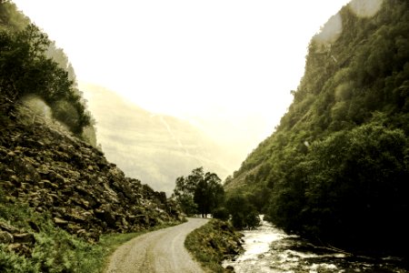 gray road beside river in the middle of green trees-covered hills