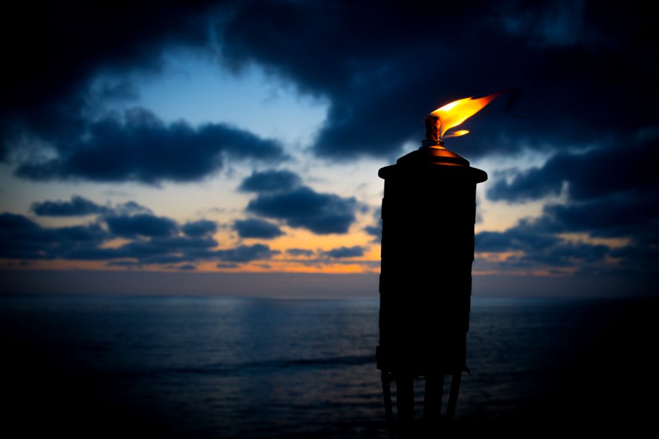lighted tiki torch near sea at night