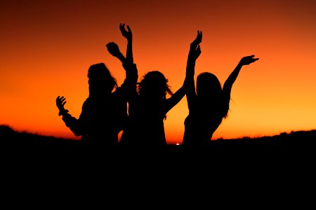 silhouette of three woman with hands on the air while dancing during sunset photo