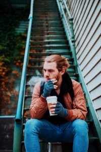 selective focus photography of man smoking while sitting on stair photo