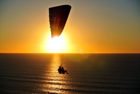 person in parachute above body of water during golden hour photo