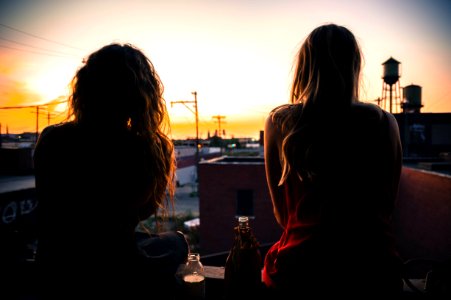 two women sitting on rooftop while watching sunset