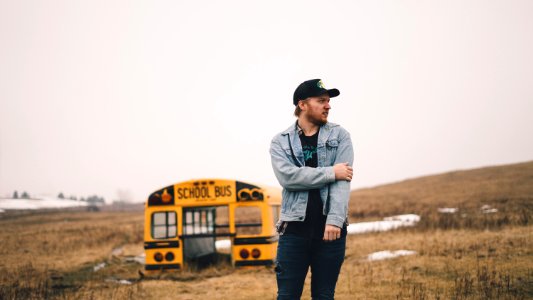 man standing on grass field near school bus part during daytime photo