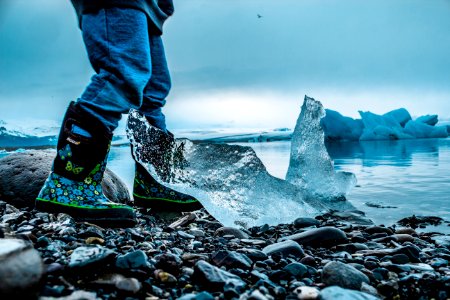 person standing on rocks beside iceberg and sea during daytime
