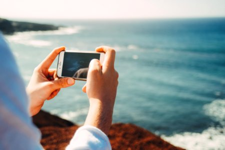 person standing on cliff taking photo of body of water during daytime photo