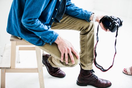 man holding DSLR camera while sitting on stool