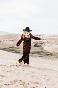photo of person wearing brown and orange floral maxi dress walking barefooted along deserted land photo