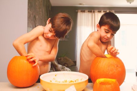 two boys holding pumpkins on table inside house photo