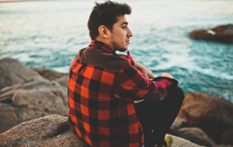 man sitting boulder near body of water photo