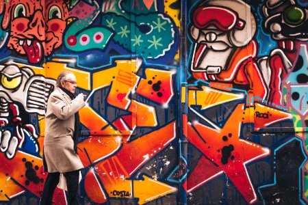 man wearing grey coat walking beside wall with graffiti