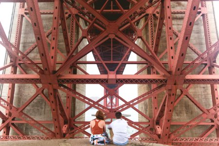 man and woman sitting near red metal scaffolding during daytime photo