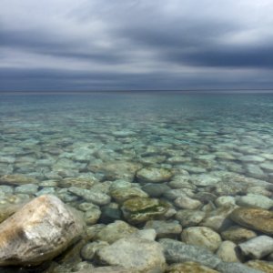 body of water with stones under cloudy sky photo