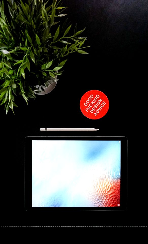 black iPad next to Apple pen near green leaf plant