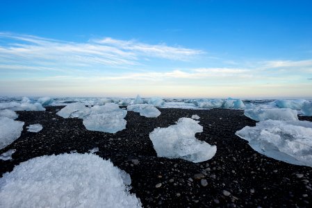 ice on black rocks under white clouds and blue sky photo