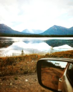 depth photography of car side mirror with a scene of body of water near mountains
