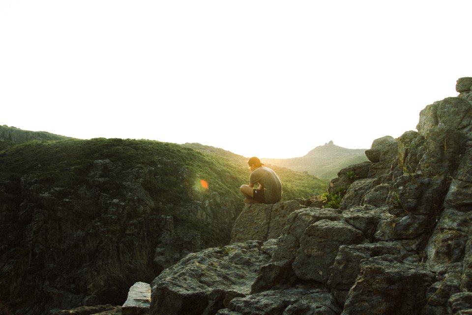 man sitting near cliff during sunrise