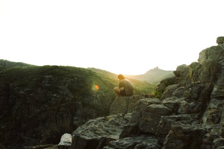 man sitting near cliff during sunrise