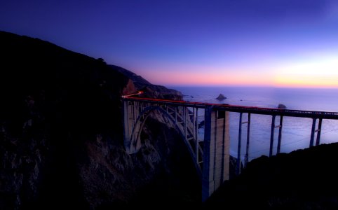 grey concrete bridge between brown and black cliff near body of water during night time photo