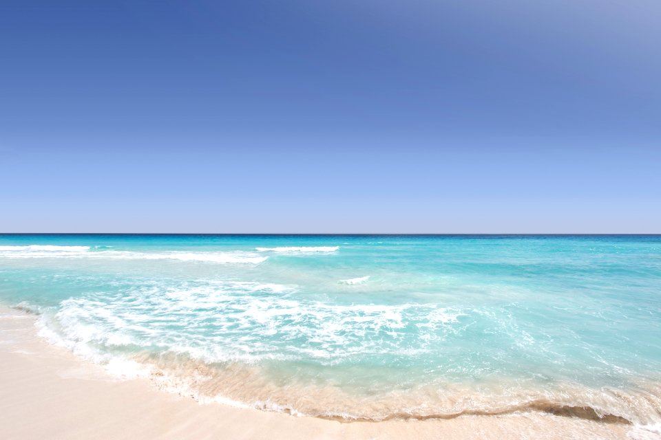 Clear blue ocean washing on the sandy shore on a clear day in Cancún