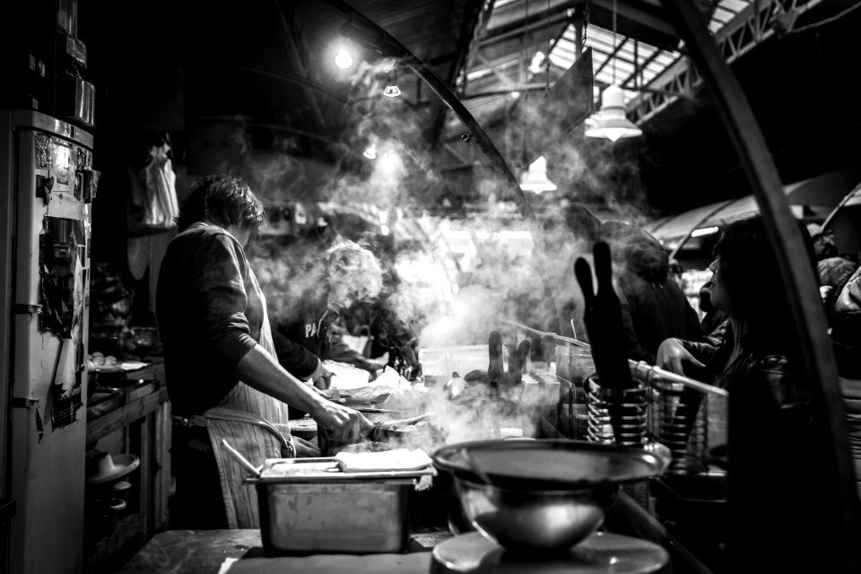 grayscale photography of man cooking beside single-door refrigerator