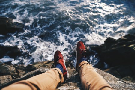 man in red sneakers sitting in cliff near body of water photo